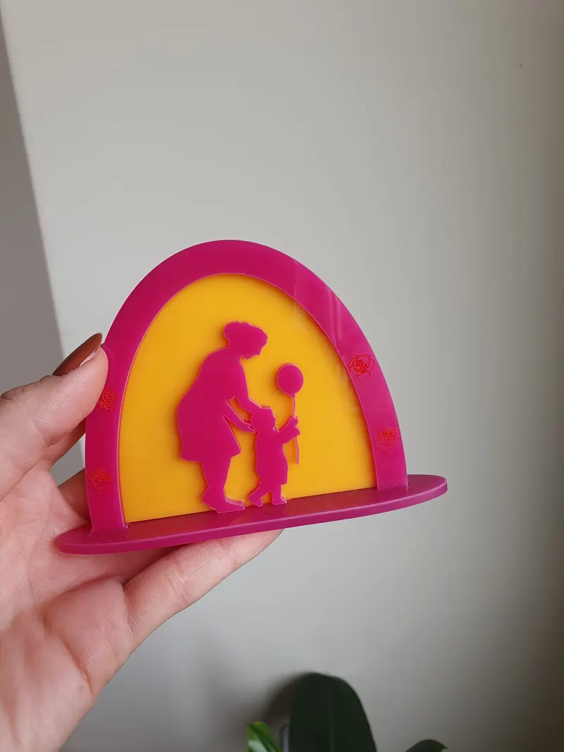 Decor din plexiglas roz și galben cu siluetele unei mame și a unui copil, pe suport